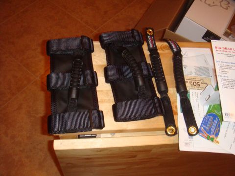 1992 Ford Bronco - Black grab handles and straps, possibly for a vehicle interior, are laid out on a wooden surface with some papers.