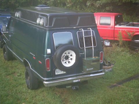 1981 Ford E350 - Green van with camper shell and spare tire, parked next to a red pickup truck.