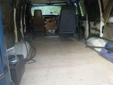 1981 Ford E350 - The interior of a van is shown, two front seats and a newly installed wooden floor, with visible insulation and wiring.