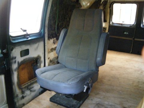 1981 Ford E350 - The interior of a van shows a single captain's chair with a worn door panel and unfinished floor.