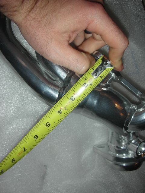 1998 Ford Crown Victoria - A hand measures an exhaust manifold pipe with a yellow tape measure.