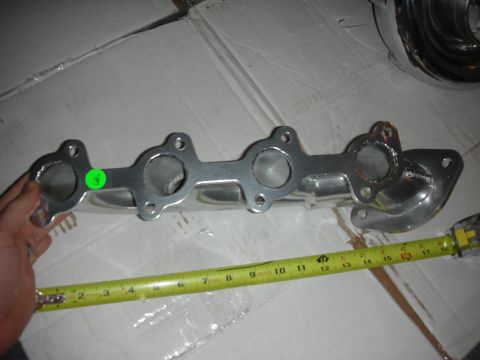 1998 Ford Crown Victoria - Chrome exhaust manifold shown with a measuring tape for size reference.
