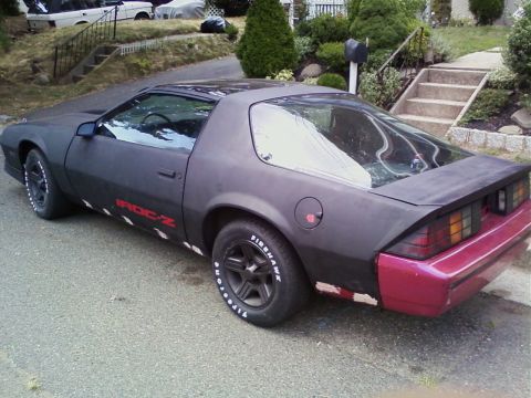 1989 Chevrolet Camaro - A matte black 1989 Chevrolet Camaro IROC-Z is seen from a 3/4 front angle with a contrasting red rear bumper.