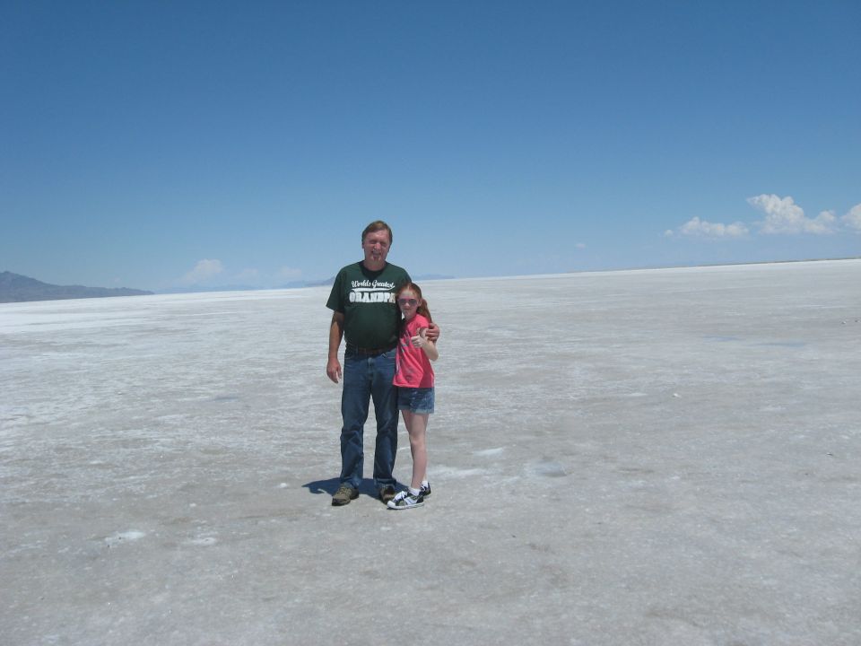 Man and young girl standing on a vast, flat, white expanse under a clear blue sky