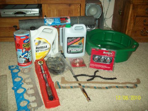 1985 Ford Bronco - Various automotive maintenance supplies and parts are organized on a carpeted surface, suggesting preparation for a vehicle service.