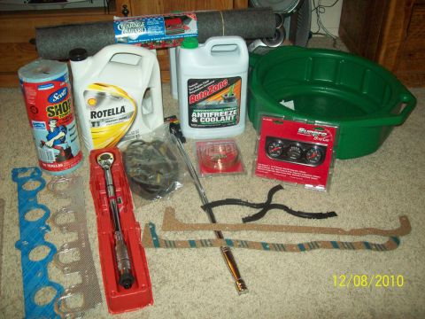 1985 Ford Bronco - A collection of automotive parts and fluids, including oil, antifreeze, a torque wrench, gaskets, and gauges, laid out on a carpeted floor.