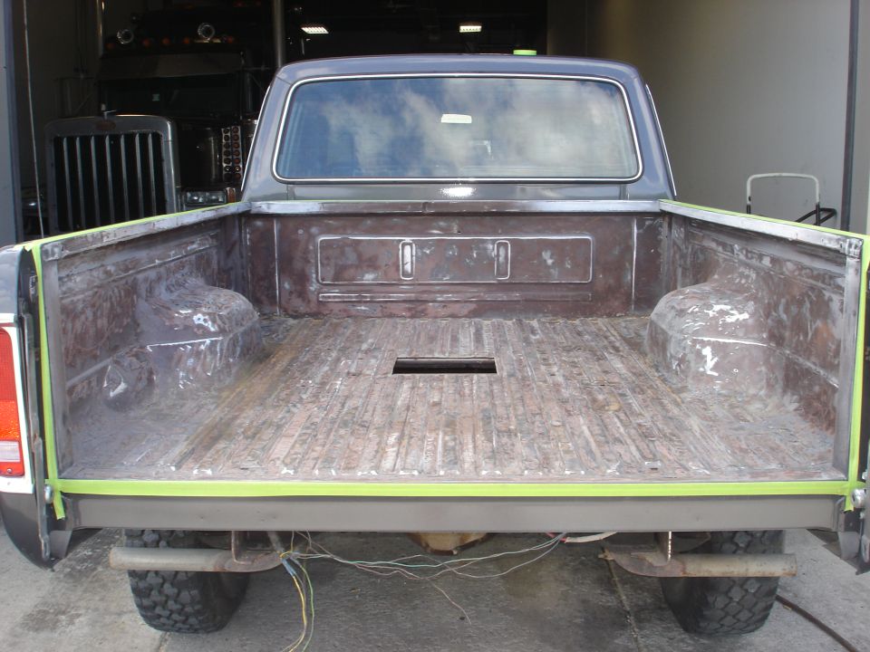 Rear view of a 1979 Ford F-250 pickup truck bed, showing exposed metal and wooden planks. Green tape is applied to the top edges of the bed