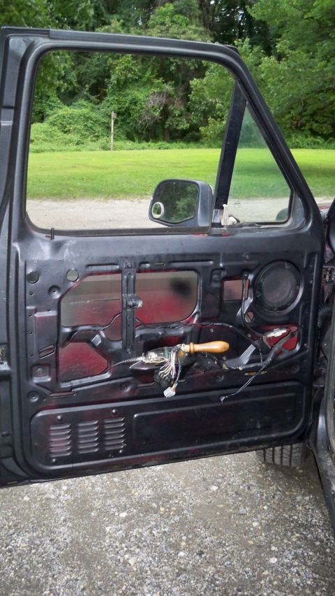 1994 Ford Bronco - The interior of an open car door reveals exposed wiring and a speaker grille.