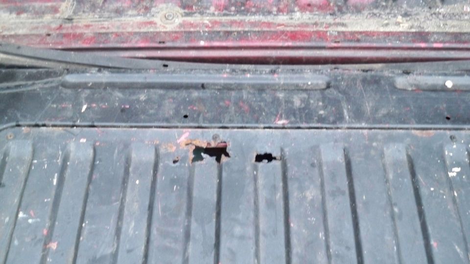 Rusted truck bed with holes and red paint visible