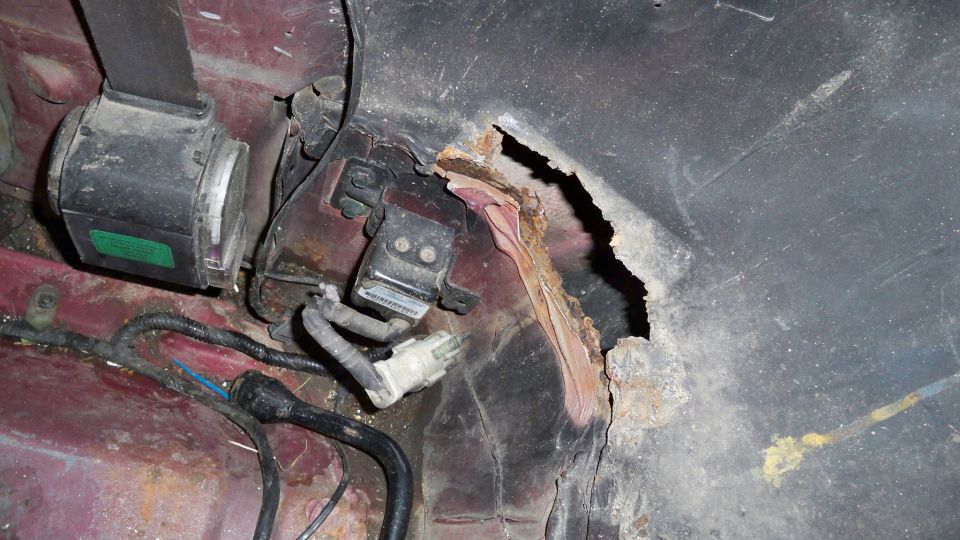 Close-up of a rusted-out wheel well with a seatbelt and wiring visible