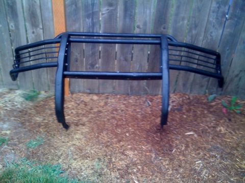1985 Ford Bronco - A black bull bar is shown leaning against a wooden fence, resting on mulch and grass.