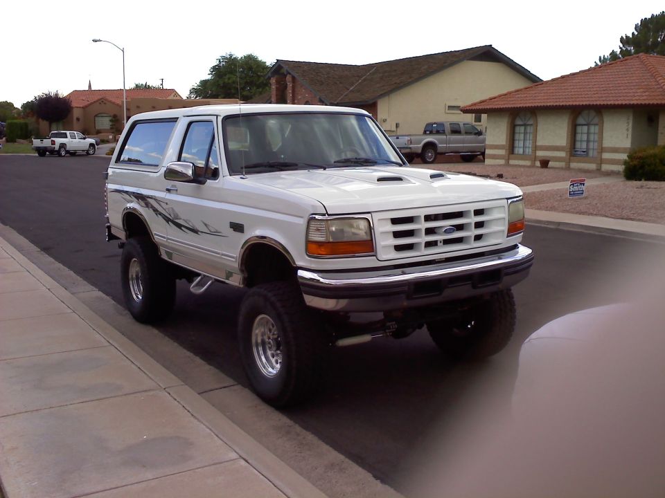 Lifted white Ford Bronco with gray splash graphics parked at a suburban curb