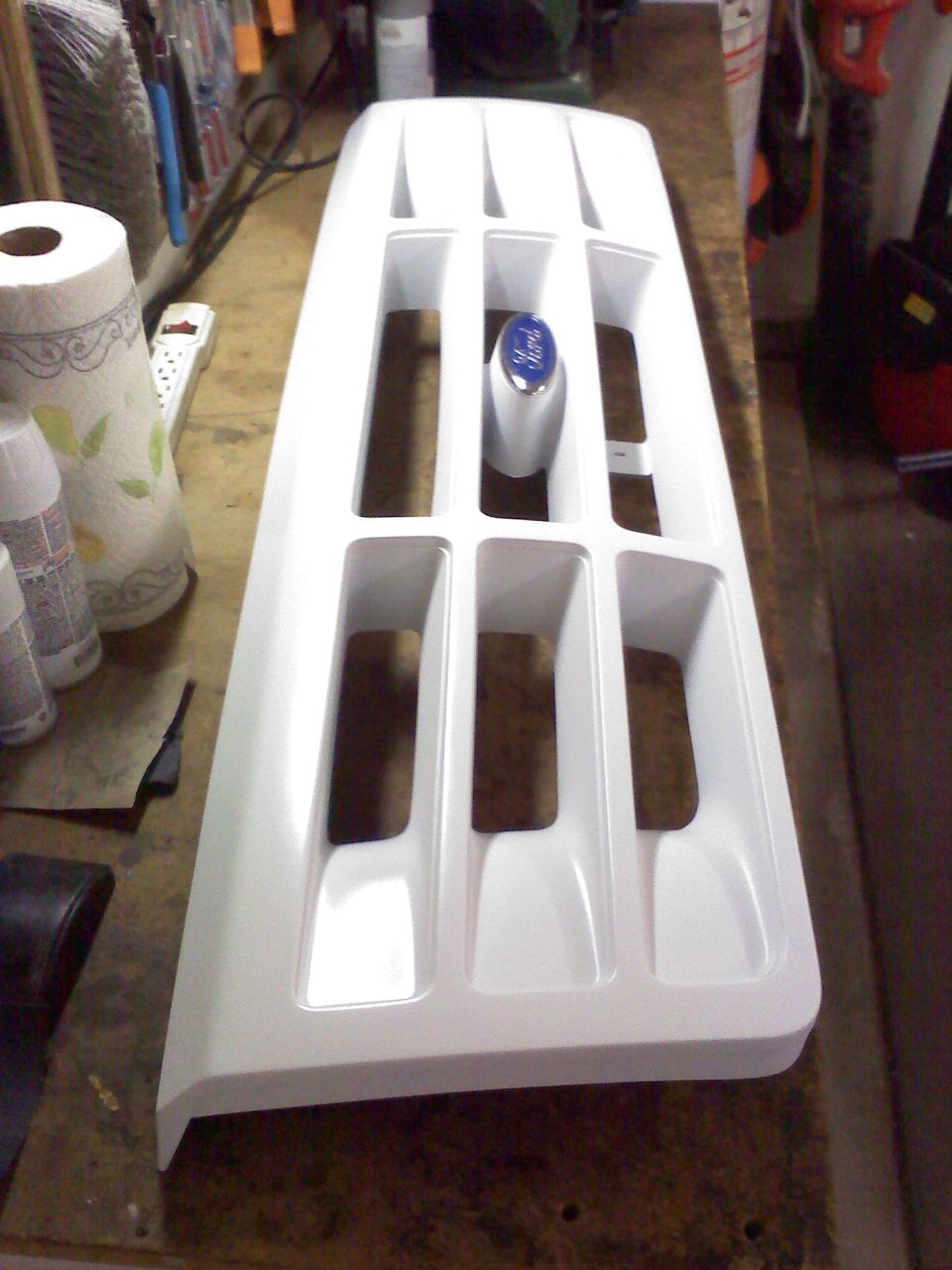 Freshly painted white Ford truck grille with blue Ford oval emblem on a workbench