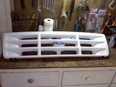 1996 Ford Bronco - White Ford Bronco grille with blue Ford oval emblem, displayed on a workbench.