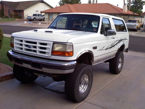 1996 Ford Bronco - A lifted white Ford Bronco is parked on a driveway, with another truck visible in the background.