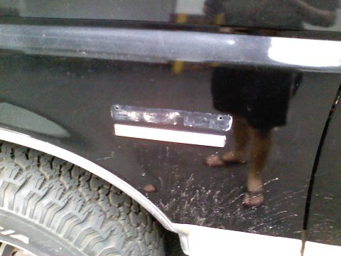 1990 Ford Bronco - Close-up of a black vehicle's side fender, revealing a tire and evidence of removed trim.