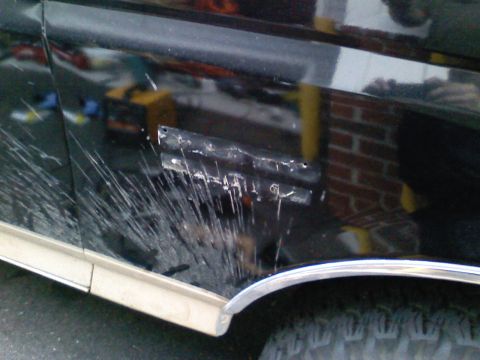 1990 Ford Bronco - Close-up of a damaged black vehicle side panel, showing extensive scratches and a dented area near the trim.