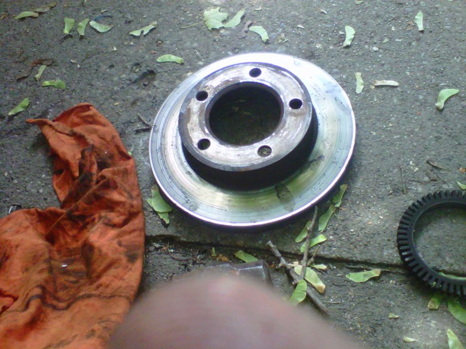 Worn used brake rotor on concrete beside a greasy rag and ABS tone ring