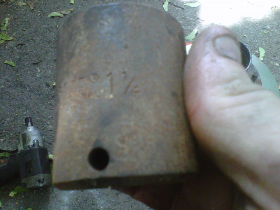 Hand holding a rusty 1-1/4 inch impact socket with an air impact wrench on the ground