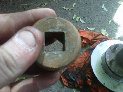 1995 Ford Bronco - A hand holds a rusty impact socket up to the camera, showing the square drive opening in its base. A brake rotor and hub with wheel studs s…