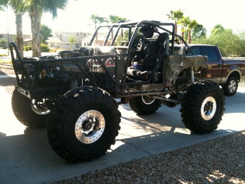 1966 Ford Bronco - A heavily modified off-road buggy with oversized tires and a custom roll cage sits beside a pickup truck.