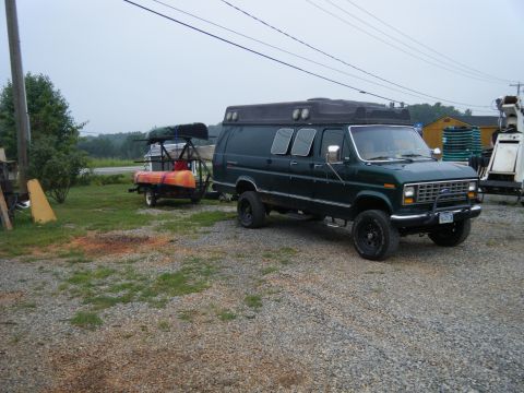 1981 Ford E350 - Van towing a trailer with kayaks, parked on a gravel lot.