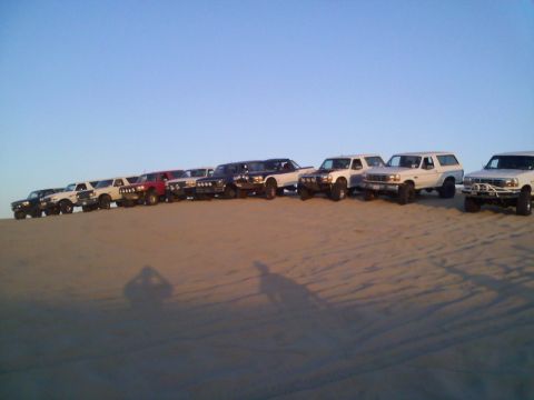 1994 Ford Bronco - Multiple Ford Broncos and trucks are lined up on a sand dune.