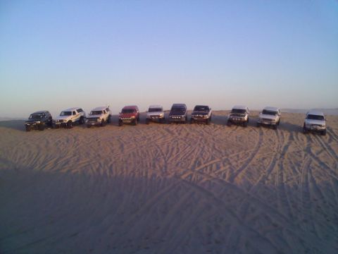 1994 Ford Bronco - A line of SUVs are parked on a sandy terrain with tire tracks visible.