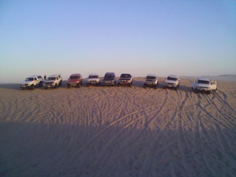 1994 Ford Bronco - Multiple SUVs are parked in a line on sand dunes, with tire tracks visible in the sand.