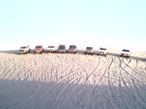 1994 Ford Bronco - A convoy of 1994 Ford Broncos traverses sandy terrain under a clear sky.