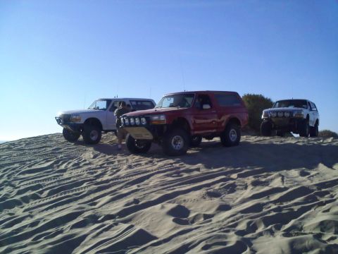 1994 Ford Bronco - Three Ford Broncos are parked on sand dunes on a sunny day.
