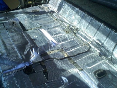 1994 Ford Bronco - The interior floor of a vehicle is covered in silver sound deadening material, with visible wiring and mounting hardware.