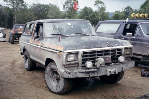 1979 Ford Bronco II - Two Ford Broncos are parked off-road, covered in mud, with one a winch and extra lights.