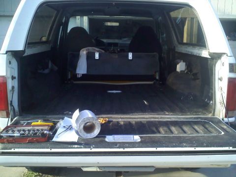 1994 Ford Bronco - The interior of a white SUV is visible with the tailgate open, revealing seats and the cargo area, along with a toolbox and roll of tape.
