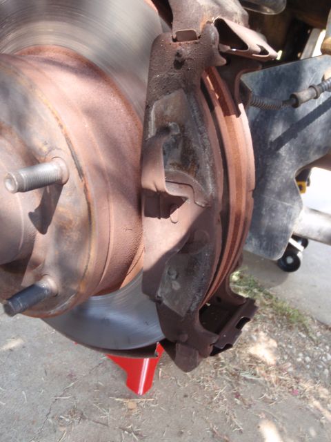 1994 Ford Bronco - Close-up of a worn brake caliper and rotor assembly, supported by a red jack stand.
