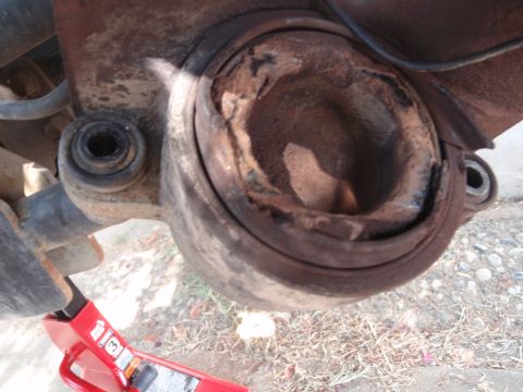 1994 Ford Bronco - Close-up of a severely worn ball joint assembly, showing significant rust and damage, with a red jack visible for support.