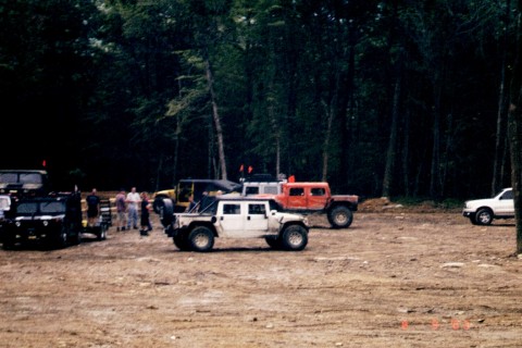 1979 Ford Bronco II - Several Humvees and a pickup truck are parked in a dirt lot near a wooded area.
