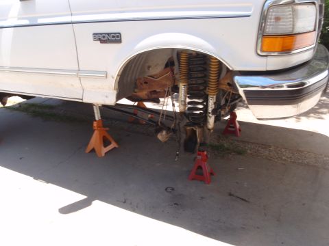 1994 Ford Bronco - The front suspension of a white Ford Bronco is exposed while it is supported by jack stands.