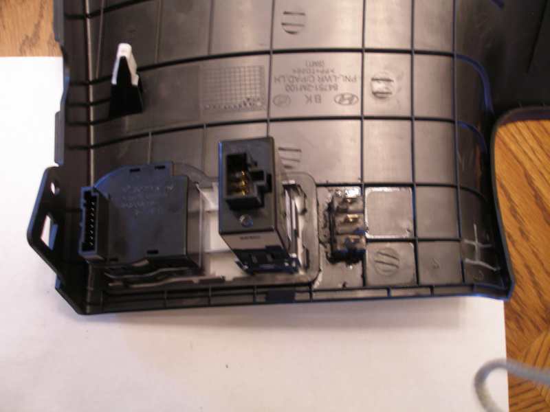 Black plastic car interior trim with electrical switches and connectors. Part number visible