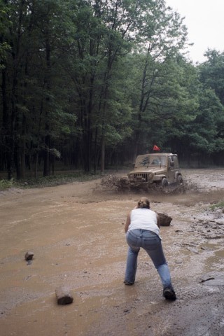 1979 Ford Bronco II - A tan SUV navigates a muddy trail, kicking up water as a person watches from the side.