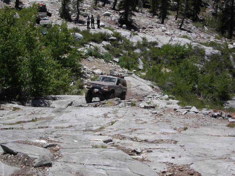Tan lifted Ford Bronco II crawling down a granite slab on a rocky mountain trail