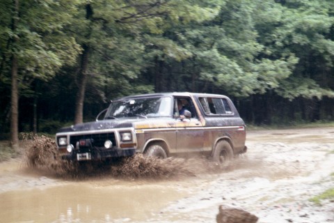 1979 Ford Bronco II - A classic Ford Bronco navigates a muddy trail, kicking up spray.