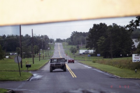 1979 Ford Bronco II - A Humvee and a red car drive down a rural road under an overcast sky.