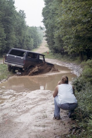 1979 Ford Bronco II - A 1979 Ford Bronco II navigates a muddy off-road trail, while a spectator observes the action.