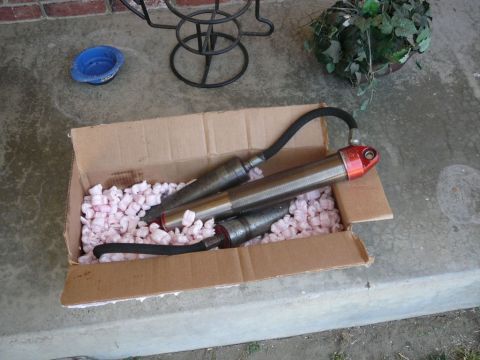 1988 Ford Bronco - Two shock absorbers are packed in a cardboard box with pink peanuts on a concrete surface.