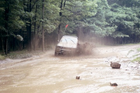 1979 Ford Bronco II - A vehicle kicks up a large spray of mud as it navigates a water-filled dirt road.