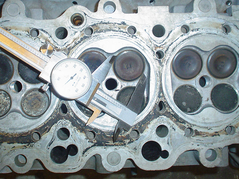 Close-up of an engine cylinder head with a caliper measuring a valve seat
