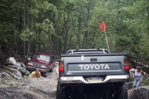 1979 Ford Bronco II - Two trucks navigate a challenging off-road course with dense forest surroundings.