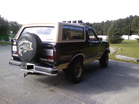 1990 Ford Bronco - This Ford Bronco is parked outdoors, showing its rear end with a spare tire cover and a two-tone paint scheme.