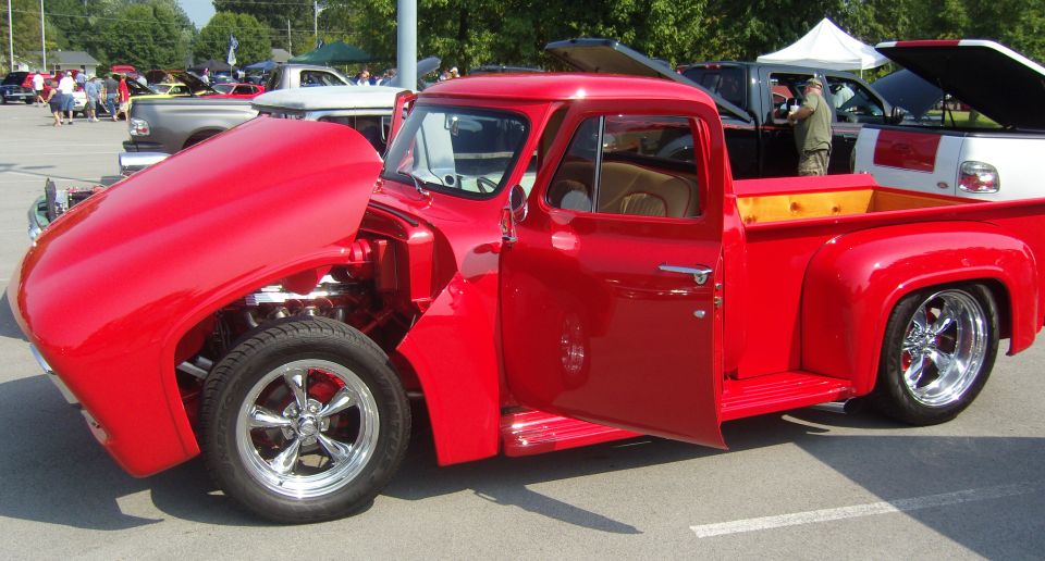 Red 1950s pickup truck with hood and driver's door open, showing engine and interior
